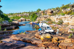 Helicopter beside a rocky waterhole in the Kimberley, with travelers nearby