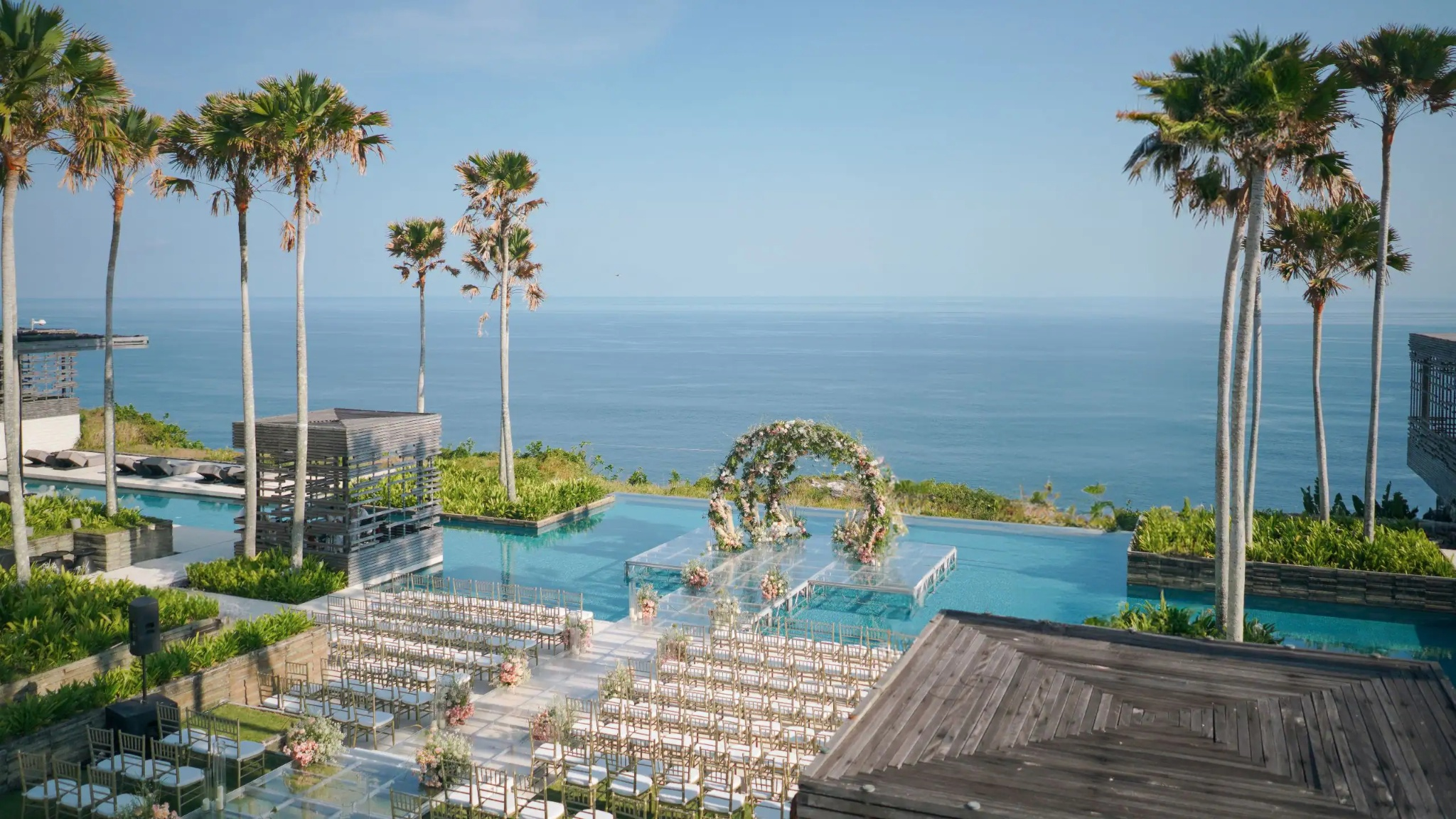 Oceanfront wedding ceremony setup with a floral arch over an infinity pool and rows of guest chairs in Bali