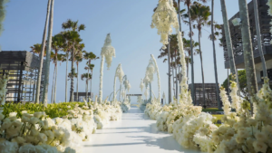 White wedding aisle lined with flowers and hanging floral decorations beneath palm trees in Bali