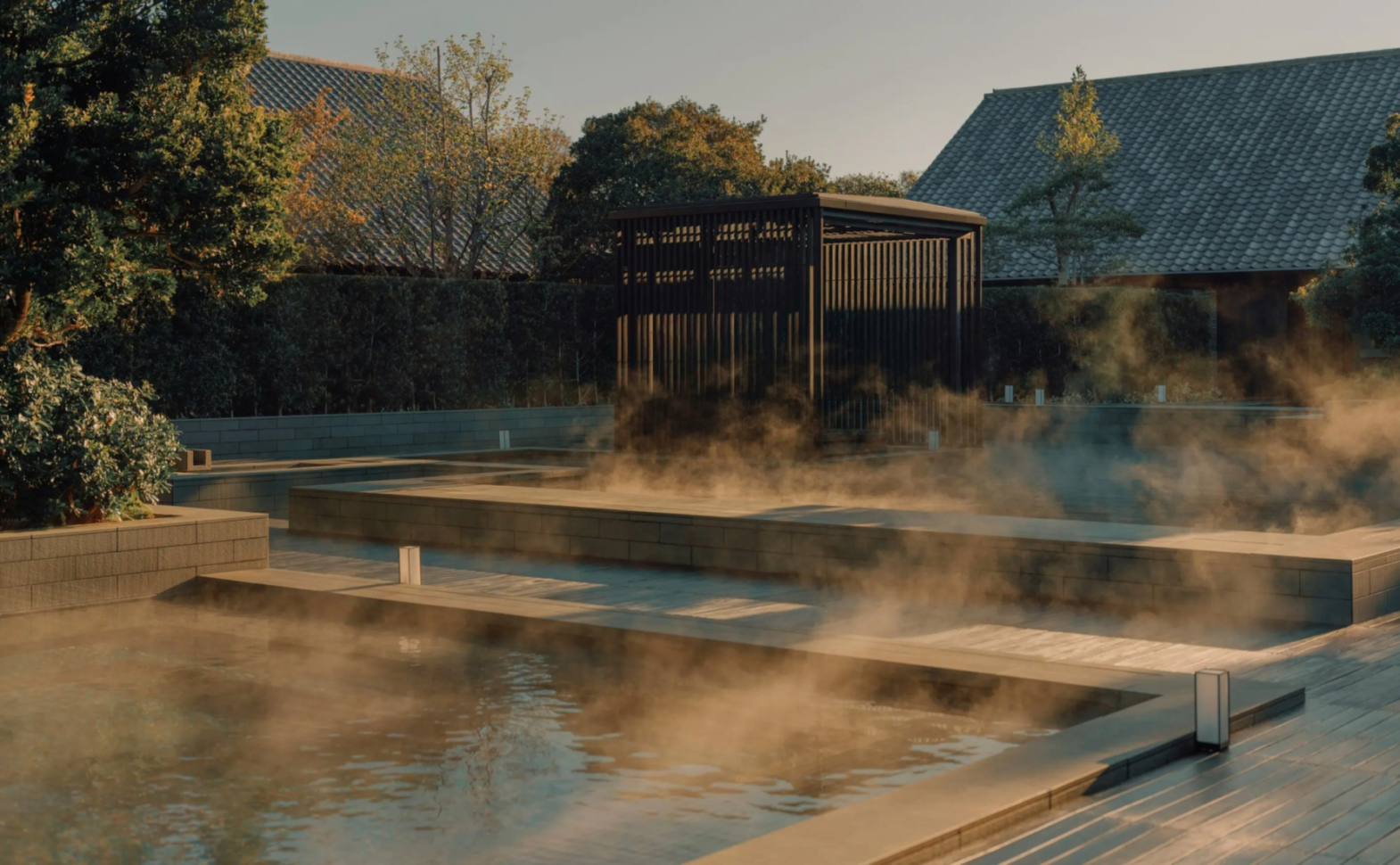 Steam rising from outdoor onsen pools at Amanemu in Ise-Shima, Japan, framed by gardens and tiled-roof bathhouses.