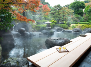Steaming outdoor foot bath at a Hoshino Resorts KAI ryokan, surrounded by rocks, autumn foliage, and a Japanese garden.