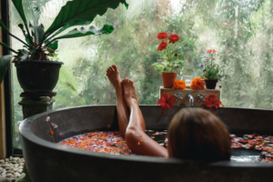 Back view woman relaxing in round outdoor bath with tropical flowers, organic skin care, luxury spa bath.